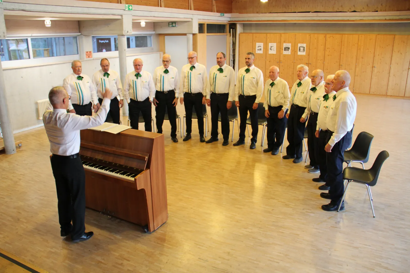 Der Dirigent leitet den Chor am Klavier in der Aula